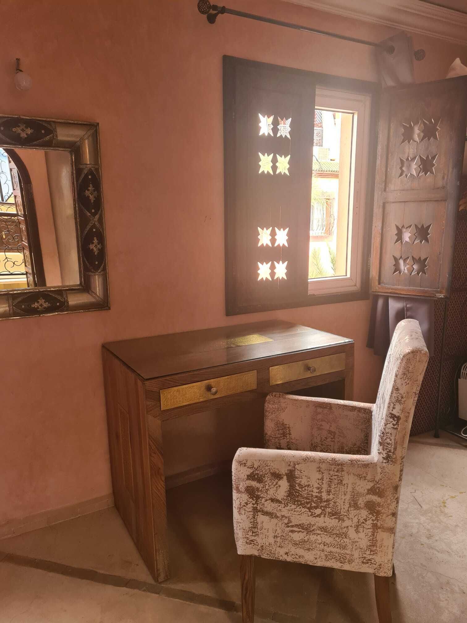 A room with a wooden desk, a chair, a mirror, and a window with decorative cutouts.