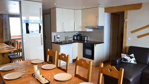 Een moderne keuken met witte kastjes, een inbouwoven en een eethoek met een houten tafel voor vier personen.