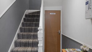 A staircase with striped carpet, a wooden door labeled "Private," and a wooden desk with a magazine and a potted plant.