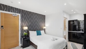 A modern hotel room with a bed, bedside tables, a nightstand, a wall-mounted TV, and a built-in microwave.