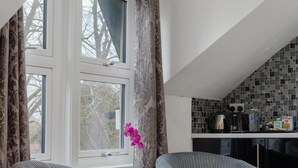 A room with two armchairs, a window with curtains, and a kitchen area with a tiled backsplash and appliances. - Modern city centre studio apartment (Oxford)