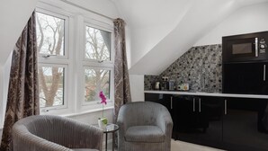 A modern kitchen with black cabinets and a microwave. There are two grey upholstered chairs and a small table with a vase of flowers. - Modern city centre studio apartment (Oxford)