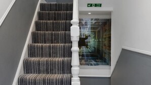 A staircase with striped carpet and white balusters, leading to a hallway with a fire exit sign. - Modern city centre studio apartment (Oxford)