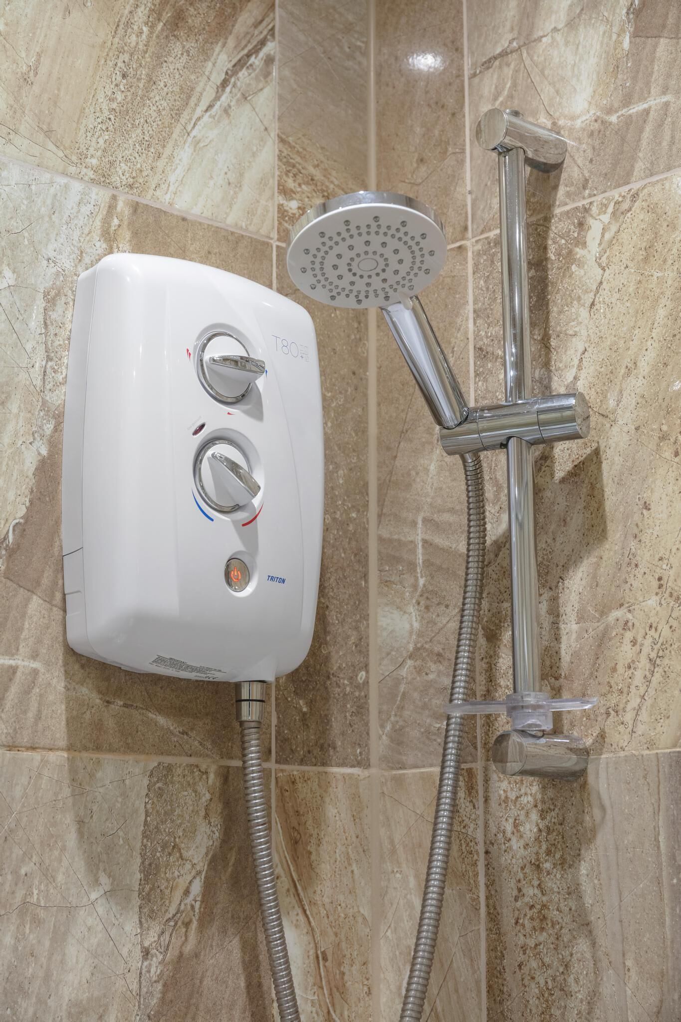 A bathroom with a white handheld showerhead, a wall-mounted faucet, and a control panel with two knobs and a power button.