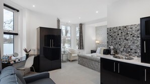 Een moderne keuken met een backsplash van natuursteen, een eethoek met een witte stoel en een zithoek met een bank en een televisie.