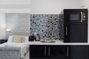 Una cocina moderna con una cama y cabecera gris con tapizado, un lavamanos y un microondas negro sobre la encimera.