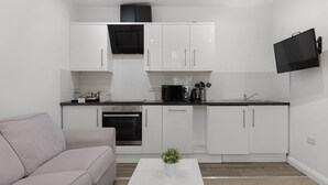 A compact kitchen with white cabinets, a built-in oven, a microwave, and a black TV mounted on the wall. - Central and Modern One Bedroom Flat (Oxford)