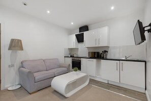 Un espace de vie compact comprenant un coin cuisine, un canapé, une table basse et un téléviseur fixé au mur.