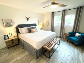 Une chambre moderne avec un lit, un banc, un fauteuil bleu et un ventilateur de plafond.