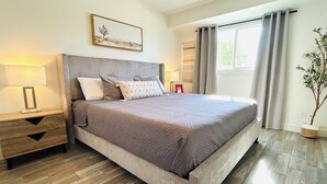 Een moderne slaapkamer met een groot bed, houten vloeren en een raam met gordijnen.