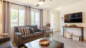 Een moderne woonkamer met een bank, fauteuils, een salontafel en een aan de muur bevestigde televisie.