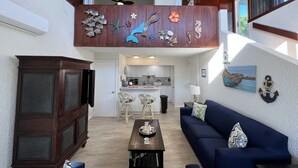 A spacious living area with a dark wooden coffee table, a blue sofa, and a kitchen in the background. - Seaside Blue <br>Hosted by Shilpi Singh (St Thomas)