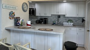 A compact kitchen with white cabinets, a microwave, a toaster, and a sink. There is a sign on the wall that reads "BEACH HOUSE". - Seaside Blue <br>Hosted by Shilpi Singh (St Thomas)