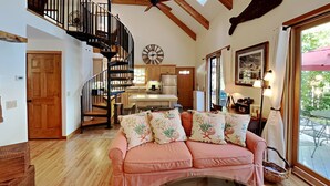 A cozy living room with a pink sofa, a wooden staircase, a kitchen area, and a large window with a view of the outdoors. - Wolfe's Way Priv. Beach, Waterfront recreation, Swim & Acadia! (Franklin)