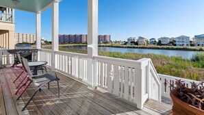 A covered outdoor area with a grill, chairs, and a view of a water body and buildings. - Aqua Easy - Destin Pointe, Gulf Views, Lakefront, Free Beach Service, Cmty Pool! (Destin)