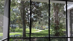 A room with large windows offering a view of a well-maintained garden and a pathway leading to a building in the distance. - Spacious 1st floor in Bahama Bay, Resort Amenities. Disney, less than 15 mins (Davenport)