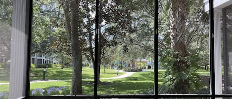 Una habitación con amplios ventanales que ofrecen vistas a un jardín cuidado y un camino que lleva a un edificio a lo lejos.