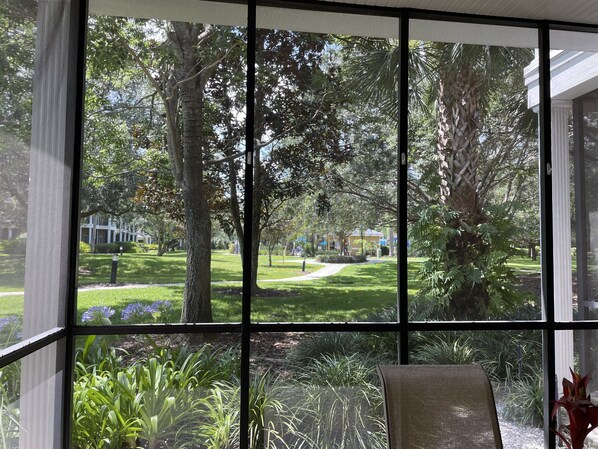Una habitación con amplios ventanales que ofrecen vistas a un jardín cuidado y un camino que lleva a un edificio a lo lejos.