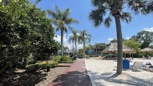 A wooden pathway leading to a beach area with palm trees and thatched umbrellas. - Spacious 1st floor in Bahama Bay, Resort Amenities. Disney, less than 15 mins (Davenport)
