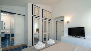 Habitación de hotel con una cama grande, televisión y baño con ducha y espejo.