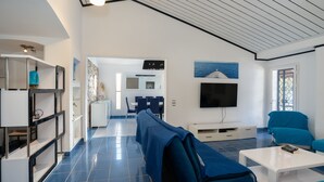 Una sala de estar moderna con techo alto, televisor de pantalla plana, sofás azules y un comedor al fondo.