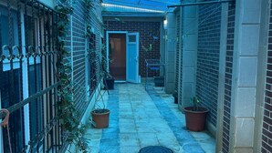 En smal, overdækket udendørs gang med flisegulv, plantekasser og en metalport på den ene side.