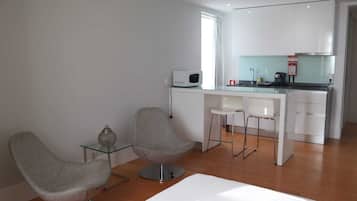 Una cocina moderna con armarios blancos, un microondas y una cafetera. Hay dos sillas grises y una pequeña mesa de vidrio con un adorno.
