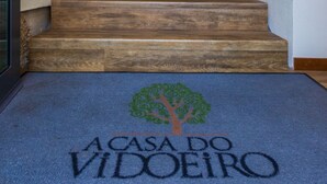 A staircase leading to an elevator with a patterned ceiling and a blue carpet with a tree and text. - Casa Do Vidoeiro (Seia)
