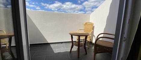 A balcony with a white wall, a tiled floor, and two wicker chairs.