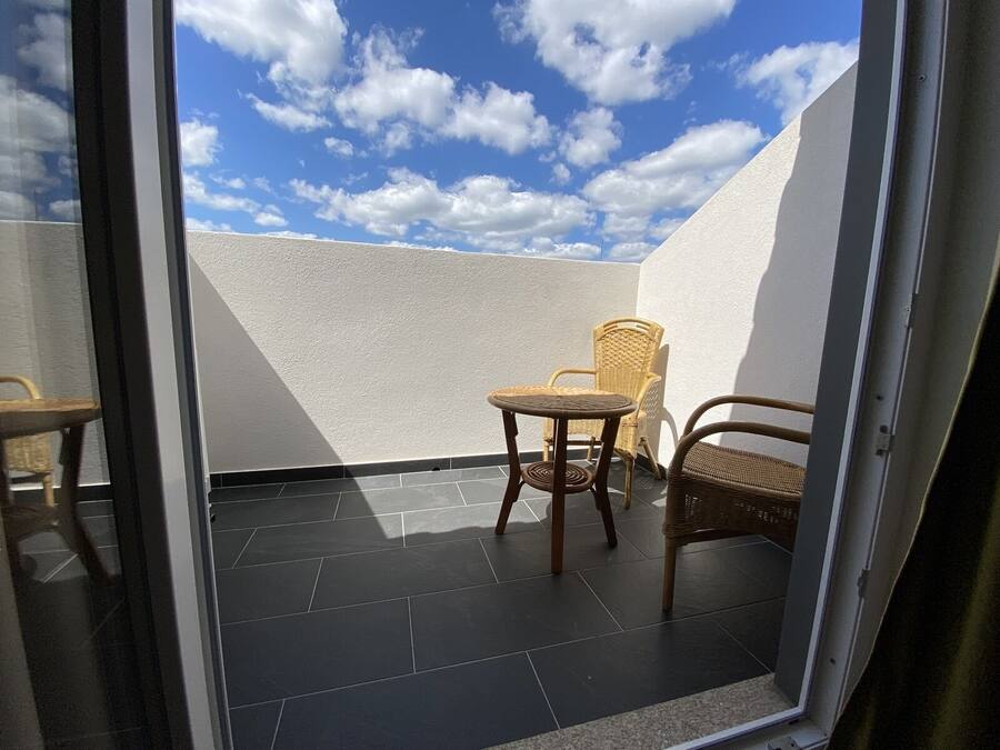 Un balcone con un muro bianco, un pavimento piastrellato e due poltrone in vimini.