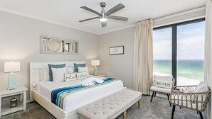 A bedroom with a bed, bedside tables, a bench, a chair, a ceiling fan, and a large window with a view of the ocean. - Salt and Sunlight: Spacious, airy 9th Floor Navarre Towers condo located on the Gulf! (Navarre)