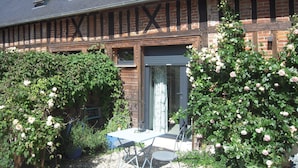 Une maison traditionnelle avec une façade en briques, une structure en poutres apparentes et un jardin où s’épanouissent des rosiers.