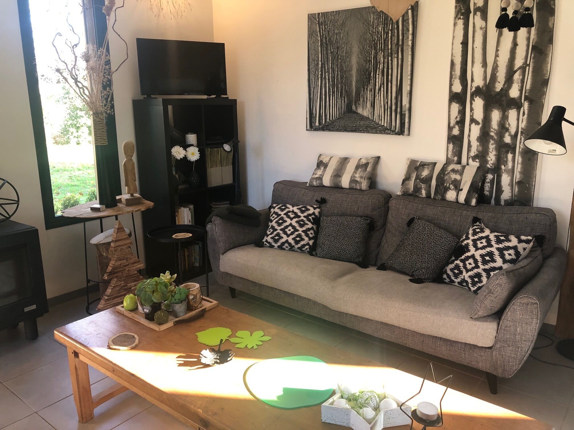 A living room with a sofa, patterned cushions, a wooden coffee table, a bookshelf, and a painting on the wall.