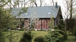 Un bâtiment traditionnel en briques, doté d’un toit en pente et de lucarnes, entouré de jardins et d’arbres bien entretenus.