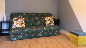A green sofa with patterned cushions in a room with wooden flooring and a dark side table. - Cosy, renovated family home in the heart of the Pyrenees (Eaux-Bonnes)