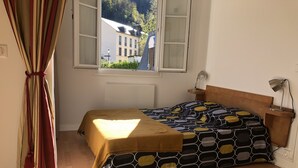 A bedroom with a bed, a window, a nightstand, and a rug. - Cosy, renovated family home in the heart of the Pyrenees (Eaux-Bonnes)