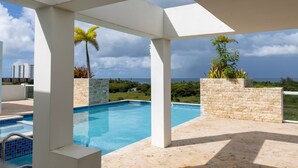 Zona de piscina con vista despejada al océano y edificios a lo lejos.