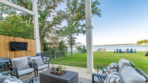 An outdoor patio with wicker furniture, a TV mounted on a wooden wall, and a view of the water.