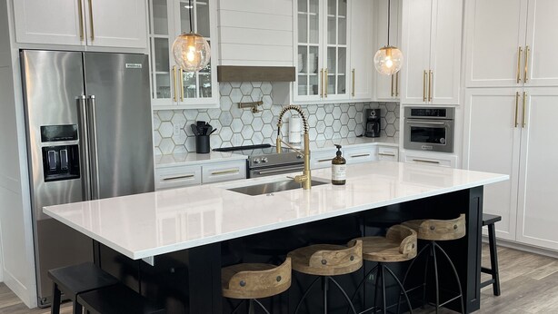 A modern kitchen with white cabinetry, a stainless steel refrigerator, a double oven, and a large island with bar stools.