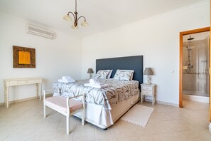 Ein Schlafzimmer mit Bett, Nachttischen, Schreibtisch, Spiegel, Dusche und einer Deckenleuchte.