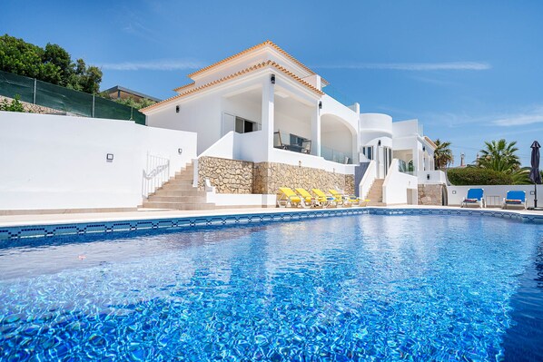 A modern villa with a swimming pool, stone walls, and a covered outdoor seating area.