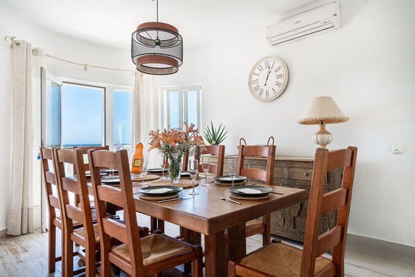 A dining area with a wooden table, chairs, a clock, and a potted plant.