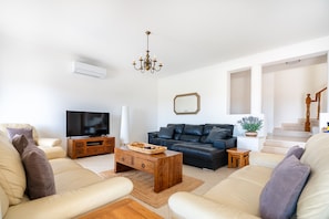 Ein Wohnzimmer mit Sofa, Fernseher, Couchtisch aus Holz und einer Kristallleuchtre.