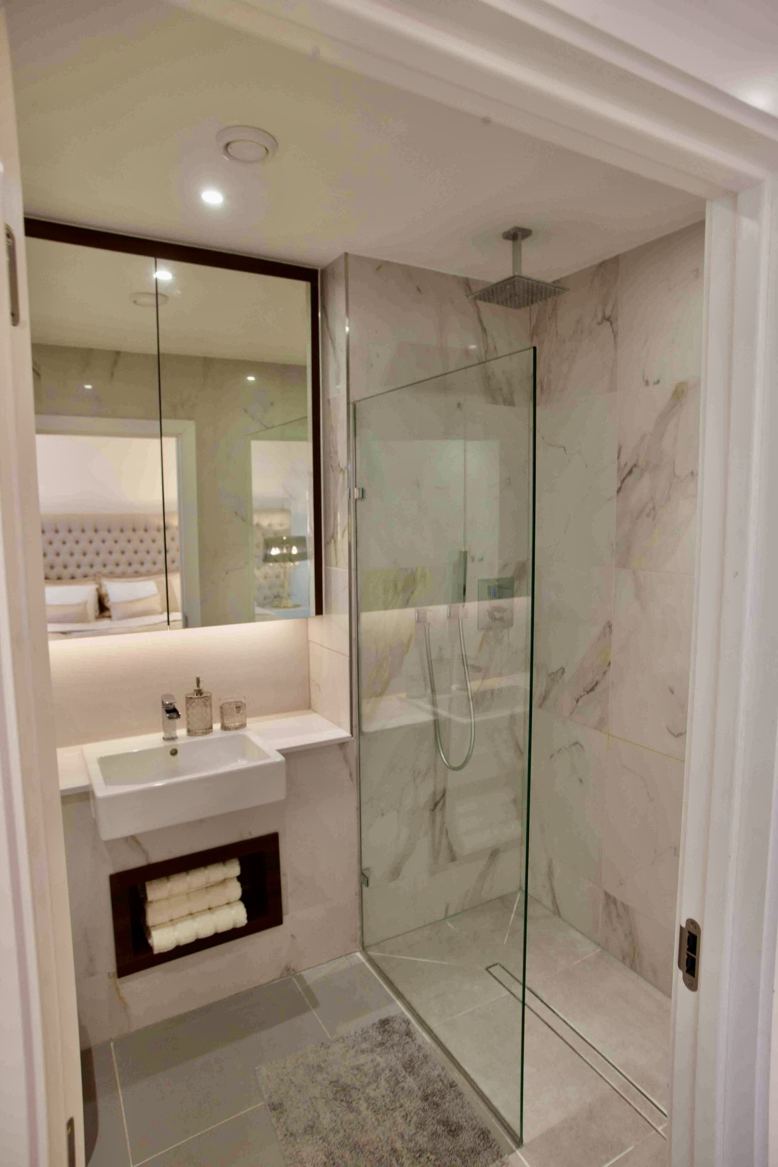 Un baño moderno con ducha envuelta en vidrio, un lavabo blanco y zona de ducha con azulejos de mármol.