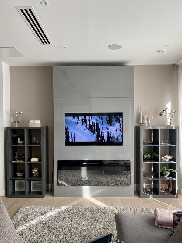 A modern living room with a flat-screen TV mounted on a grey wall, surrounded by shelves and a fireplace. - Thames Riverside Apartment in London (London)