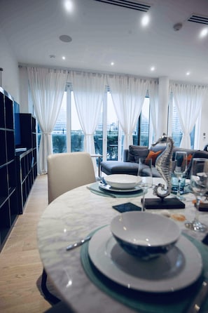 A modern dining area with a round table set for four, a sofa, and a bookshelf. - Thames Riverside Apartment in London (London)