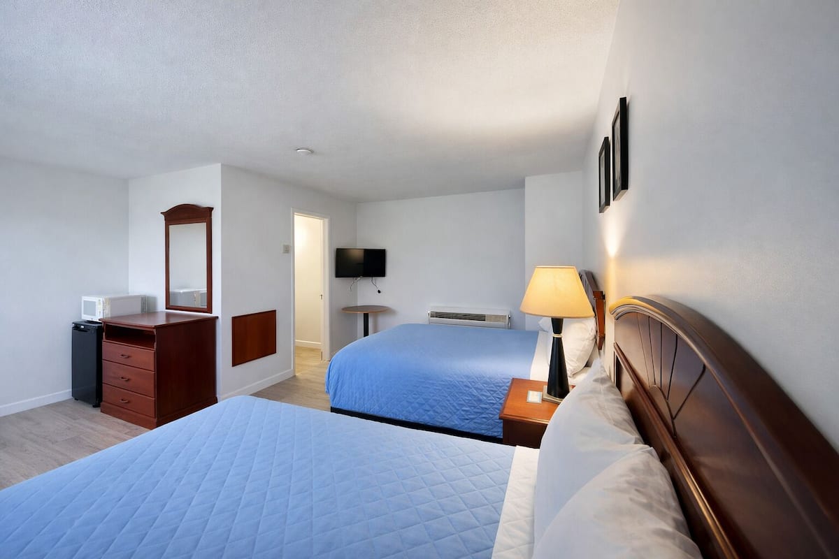 A hotel room with two beds, a dresser, a TV, and a lamp.