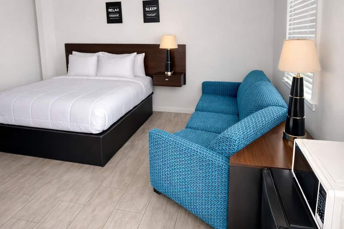 A hotel room with a bed, a blue sofa, a small table with a lamp, a microwave, and two wall-mounted signs.
