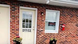 A brick building with a white door labeled 'OFFICE,' a fire extinguisher mounted on the wall, and two flower planters on the sidewalk. - Relax Inn Smyrna Dover Coastal Gateway (Smyrna)