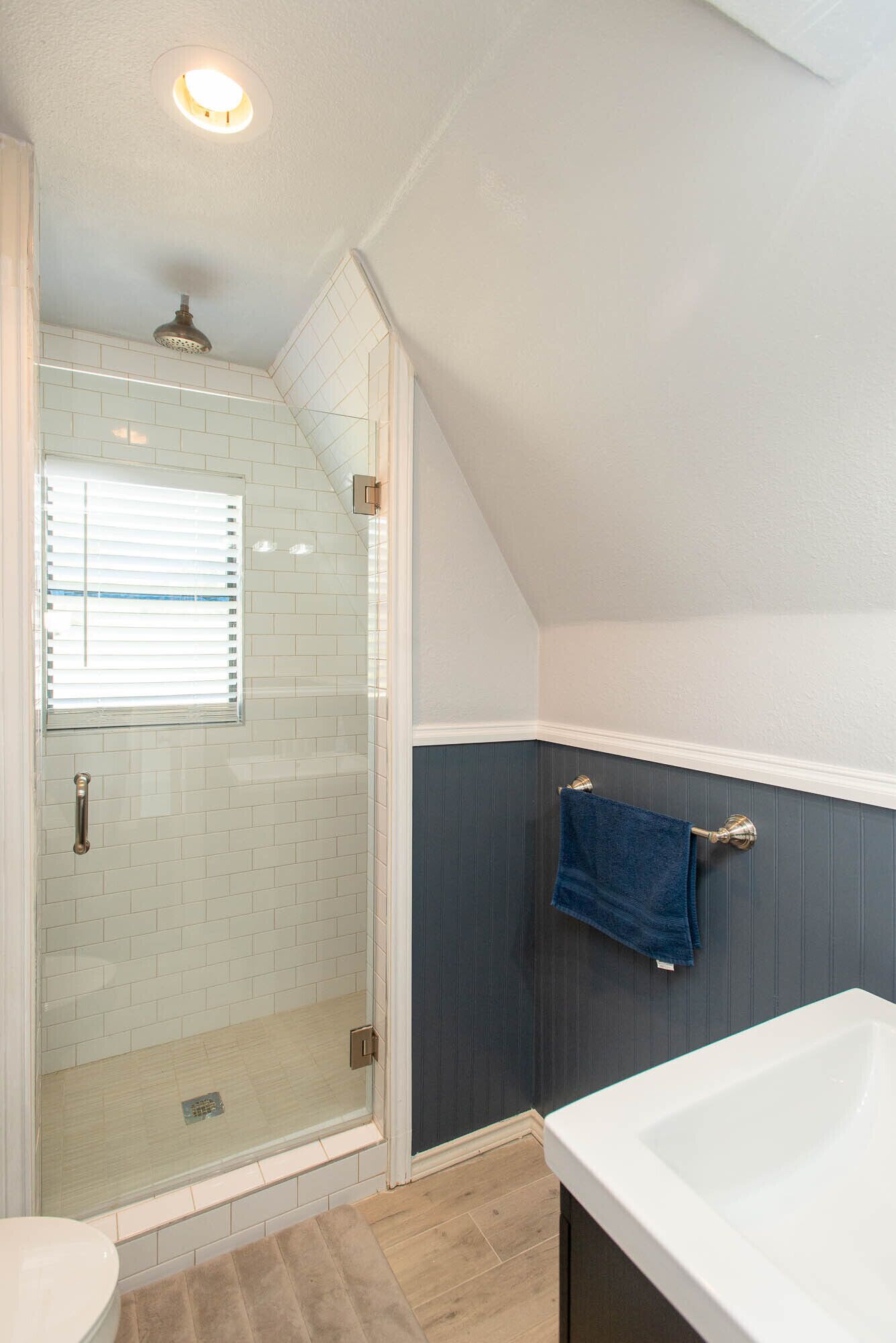 A bathroom with a glass shower enclosure, a bathtub, and a window with blinds.